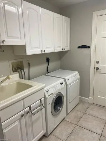 Clothes washing area featuring light tile patterned flooring, a sink, baseboards, washer and dryer, and cabinet space