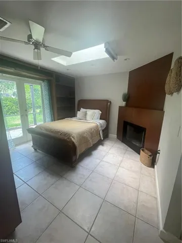 Tiled bedroom featuring access to exterior, a ceiling fan, a skylight, a large fireplace, and visible vents
