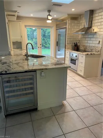 Kitchen featuring beverage cooler, light stone counters, oven, fridge, and exhaust hood