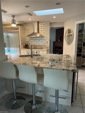 Kitchen featuring a breakfast bar area, decorative backsplash, a sink, ventilation hood, and light stone countertops