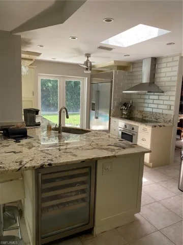 Kitchen featuring wine cooler, sink, fridge, wall oven, and range hood