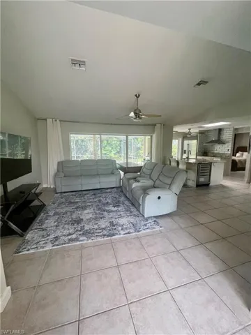 Unfurnished living room with ceiling fan, visible vents, vaulted ceiling, and light tile patterned floors