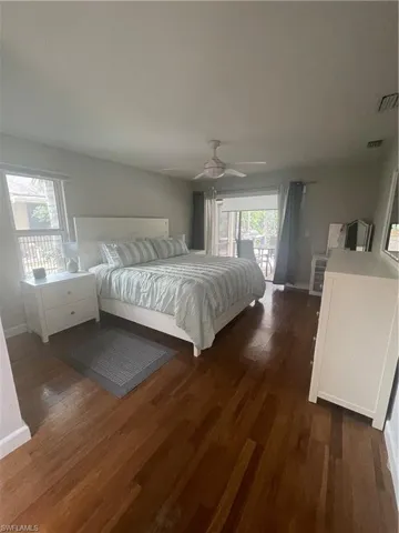 Bedroom with access to outside, dark wood finished floors, baseboards, visible vents, and ceiling fan