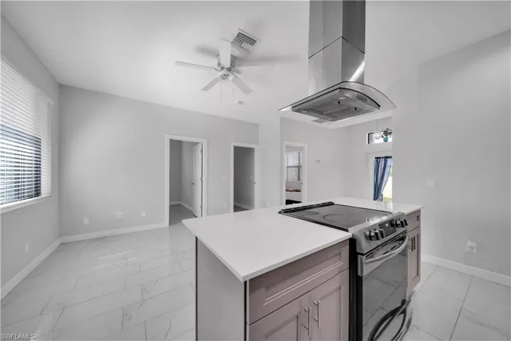 Kitchen island with built-in range, stainless steel range hood, and white countertops