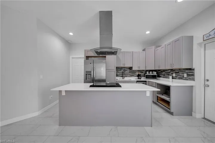 Modern kitchen featuring a central island with an integrated cooktop, stainless steel appliances, extensive cabinetry with brushed nickel hardware, a tile backsplash, and recessed lighting