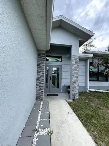 Front entry featuring double glass doors, stone facade accents, stucco exterior, and a concrete pathway with stepping stones
