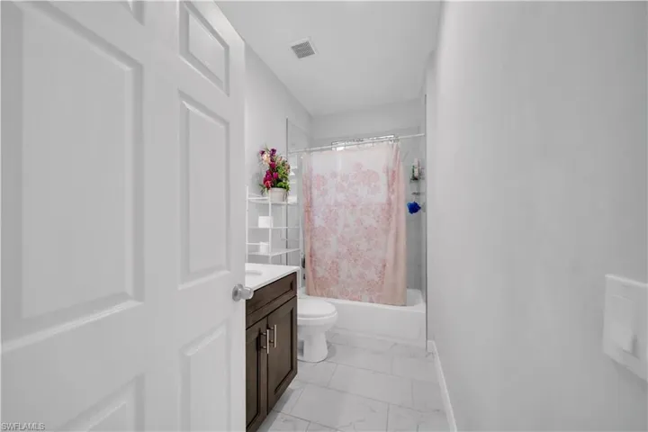 Bathroom featuring a white paneled door, dark wood-finish vanity with white countertop, white toilet, and a white tub with shower