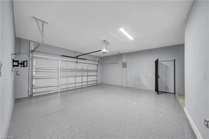 Spacious garage featuring a finished epoxy floor, white paneled garage door, and a dedicated side entry door