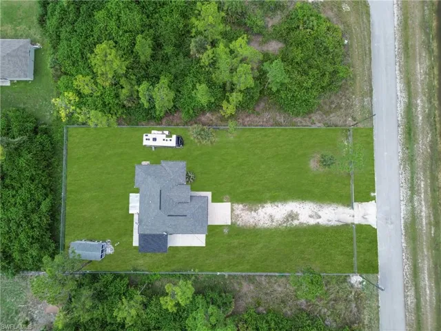 Expansive property featuring a dark-shingled roofline, green lawn, a detached storage shed, a paved drive, and surrounding natural foliage