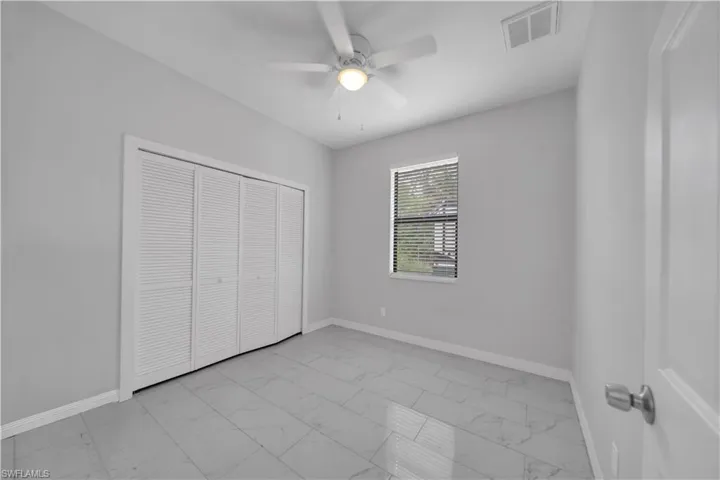 Neutral-toned interior room featuring light gray walls, large format floor tiling, a white ceiling fan with integrated lighting, and a window with blinds