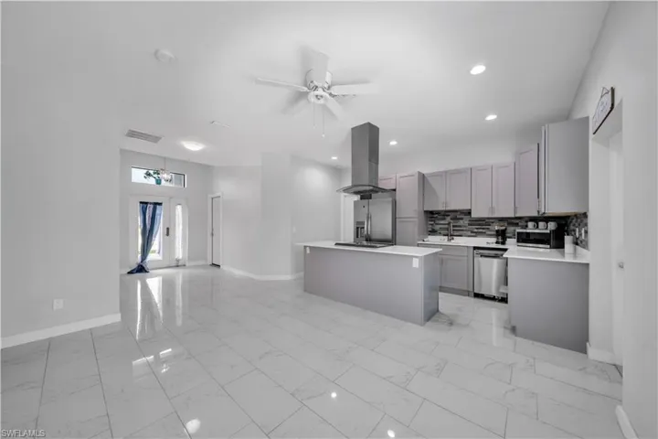 Open-concept kitchen featuring an island, stainless steel appliances, grey cabinetry, and a tile backsplash