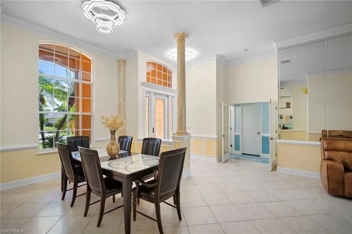Dining room with decorative columns, crown molding, light tile patterned floors, a towering ceiling, and french doors