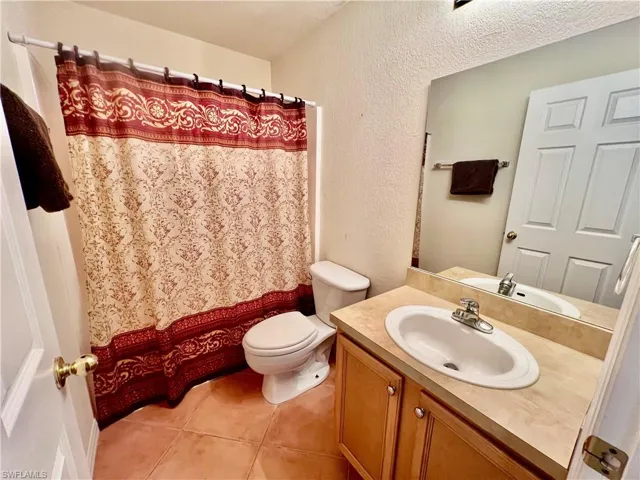 Full bathroom featuring tile patterned floors, a shower with shower curtain, toilet, vanity, and a textured wall