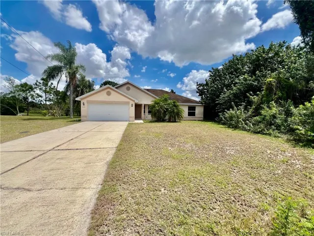 Ranch-style house with stucco siding, a garage, a front lawn, and an extra long concrete driveway with plenty of parking.