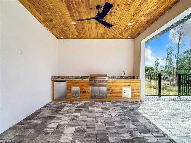 View of patio featuring exterior kitchen, sink, a grill, and ceiling fan