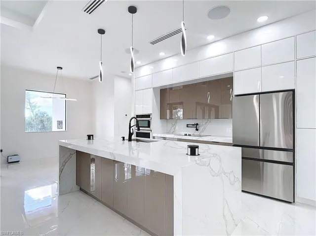 Kitchen with sink, hanging light fixtures, white cabinetry, a large island, and stainless steel appliances