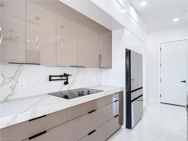 Kitchen featuring gray cabinets, fridge, light stone countertops, and black electric cooktop