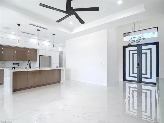 Kitchen featuring a spacious island, a raised ceiling, pendant lighting, and ceiling fan with notable chandelier