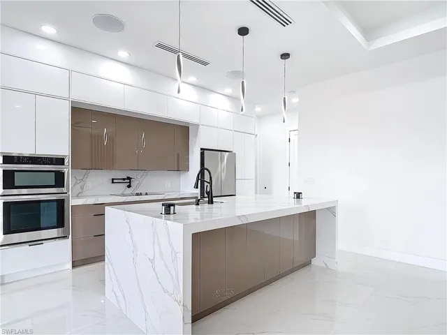 Kitchen featuring sink, hanging light fixtures, a large island, stainless steel appliances, and white cabinets