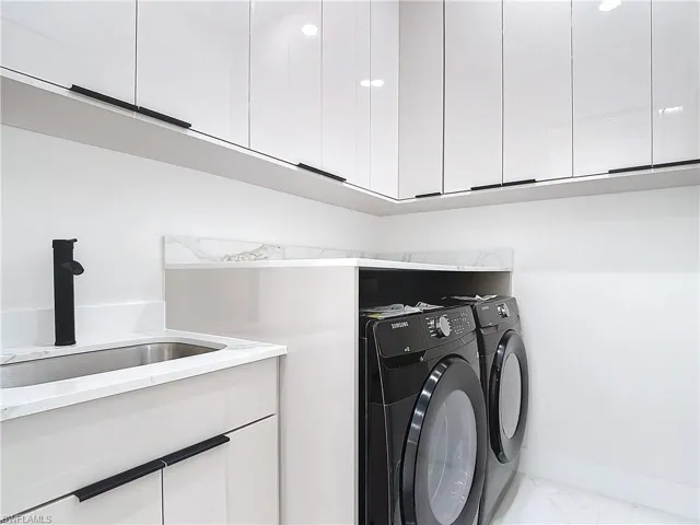 Laundry room featuring sink, washing machine and dryer, and cabinets