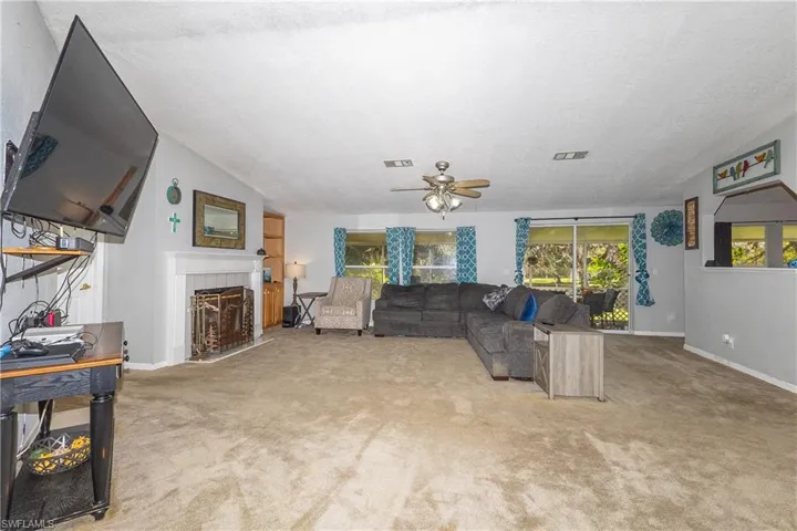 Living room with a tiled fireplace, light colored carpet, ceiling fan, and lofted ceiling