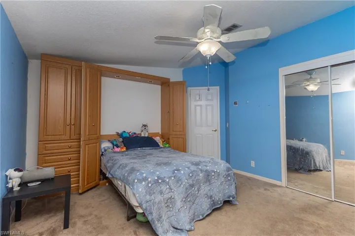 Bedroom featuring light colored carpet, lofted ceiling, a closet, a ceiling fan, and a textured ceiling