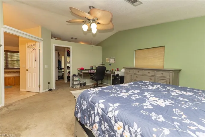 Bedroom featuring an office area, lofted ceiling, a walk in closet, carpet floors, and a ceiling fan
