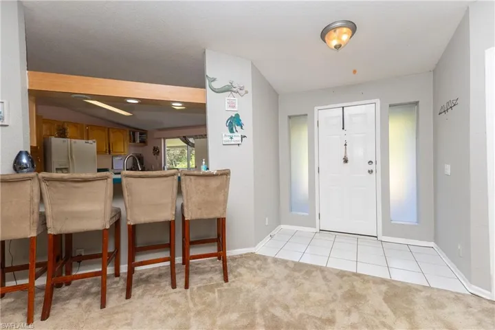 Foyer entrance with light tile patterned floors, light colored carpet, and lofted ceiling