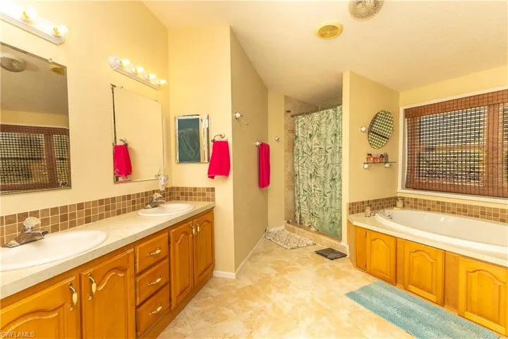 Full bath with a stall shower, a garden tub, double vanity, tasteful backsplash, and a textured ceiling