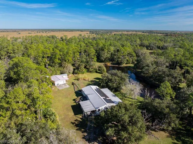 Aerial view of property and surrounding area with a nearby body of water and a heavily wooded area