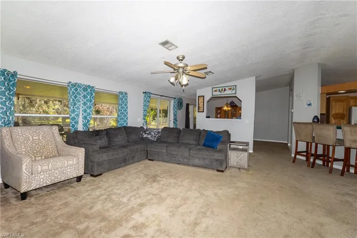 Living area with a ceiling fan, light carpet, and a textured ceiling