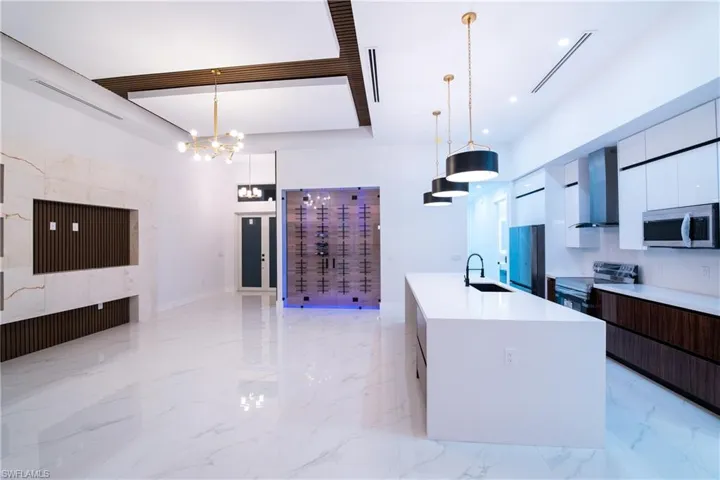 Kitchen featuring appliances with stainless steel finishes, a kitchen island with sink, pendant lighting, and wall chimney exhaust hood