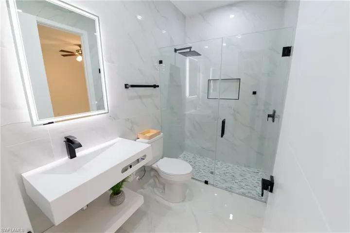 Bathroom with a shower with shower door, sink, tile walls, and toilet