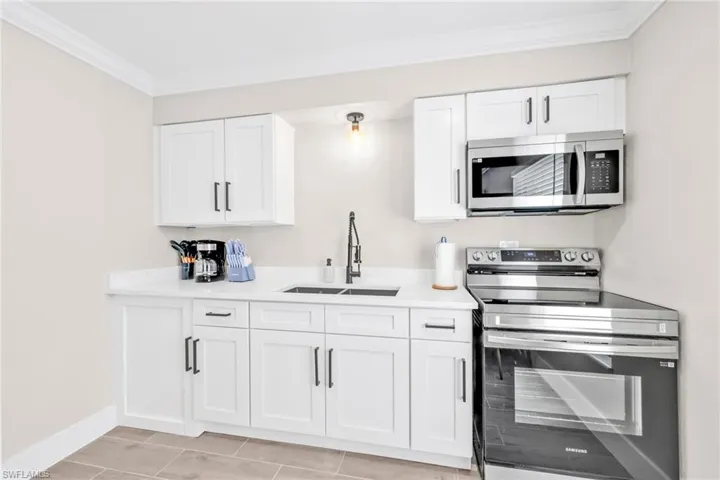 Kitchen with stainless steel appliances, white cabinetry, crown molding, and light stone counters