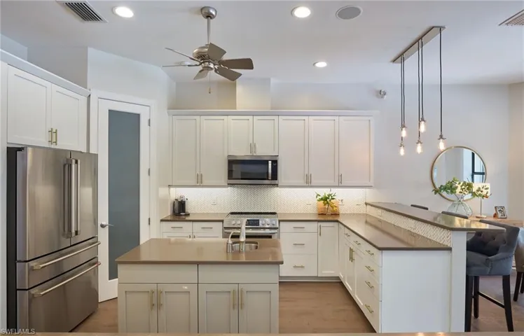 Kitchen with hanging light fixtures, white cabinetry, an island with sink, premium appliances, and ceiling fan