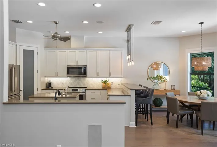 Kitchen featuring hanging light fixtures, high end appliances, kitchen peninsula, dark wood-type flooring, and white cabinetry