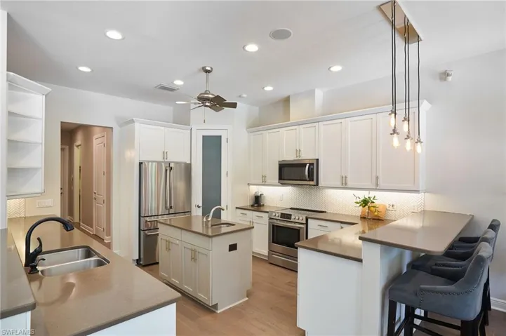 Kitchen featuring sink, white cabinetry, kitchen peninsula, hanging light fixtures, and stainless steel appliances