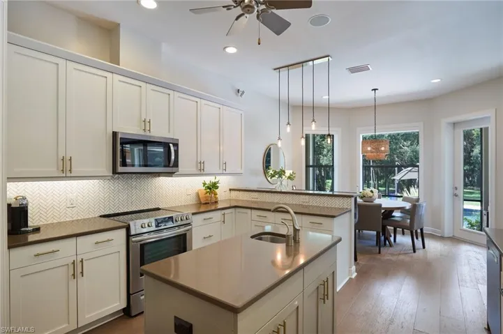 Kitchen with sink, kitchen peninsula, appliances with stainless steel finishes, decorative light fixtures, and ceiling fan