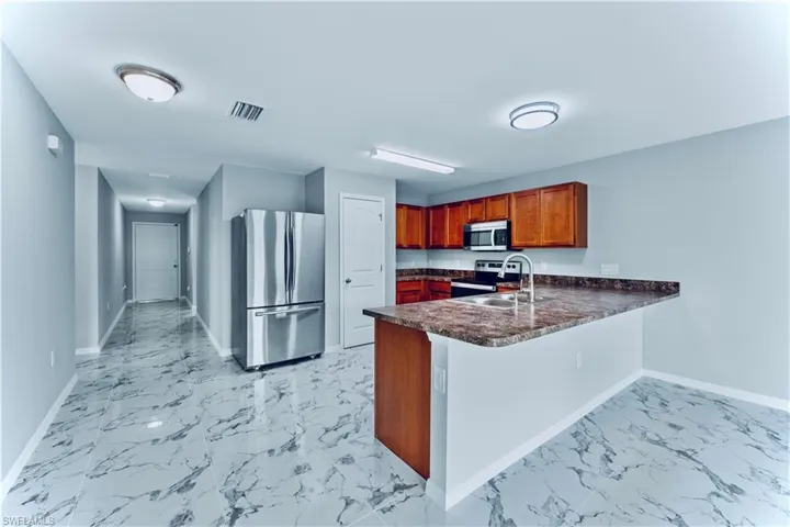 Kitchen with appliances with stainless steel finishes, sink, light tile floors, and kitchen peninsula
