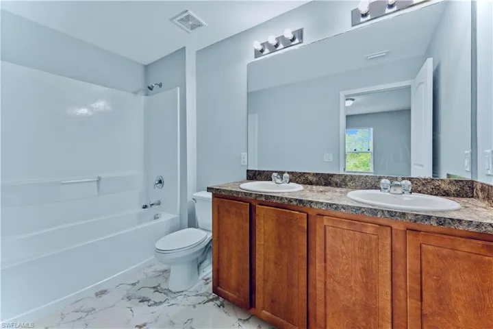 Full bathroom with tile floors, dual bowl vanity, shower / tub combination, and toilet