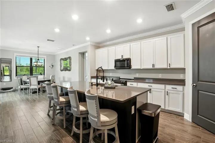 Kitchen with ornamental molding, dark wood-type flooring, white cabinetry, decorative light fixtures, and a breakfast bar