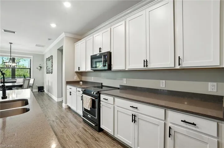 Kitchen with black appliances, dark stone countertops, crown molding, white cabinetry, and decorative light fixtures