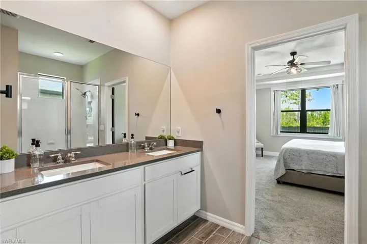 Ensuite bathroom featuring a stall shower, double vanity, wood finish floors, and a ceiling fan