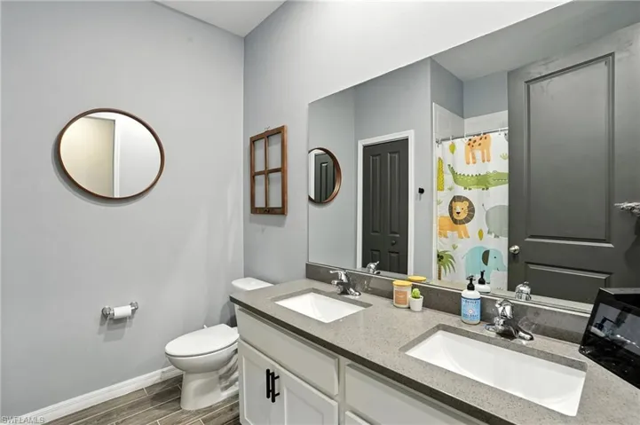 Full bathroom with double vanity, wood finish floors, and a shower with curtain