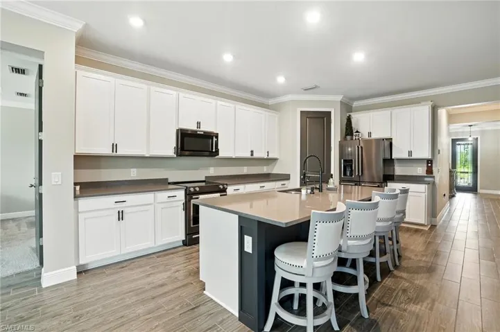 Kitchen featuring ornamental molding, appliances with stainless steel finishes, white cabinetry, a kitchen breakfast bar, and an island with sink