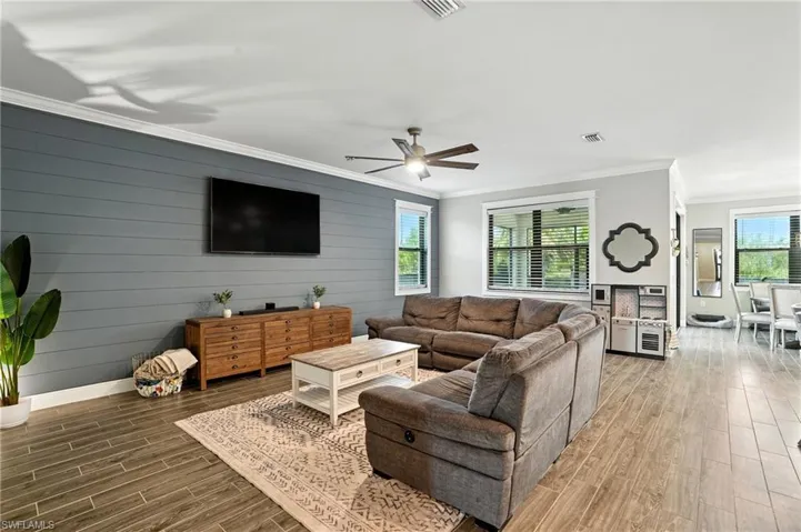 Living area with ornamental molding, plenty of natural light, wood tiled floors, a ceiling fan, and wood walls