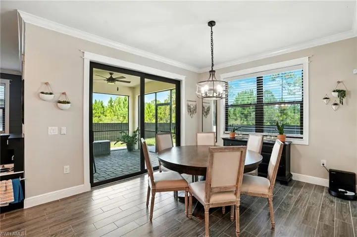Dining room with ornamental molding, wood tiled floors, healthy amount of natural light, ceiling fan, and a chandelier