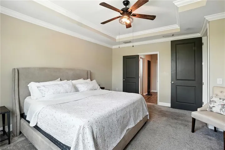Carpeted bedroom featuring a tray ceiling, crown molding, and a ceiling fan