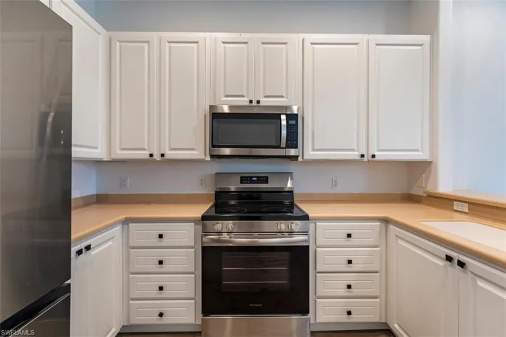 Kitchen with stainless steel appliances, white cabinetry, and light countertops