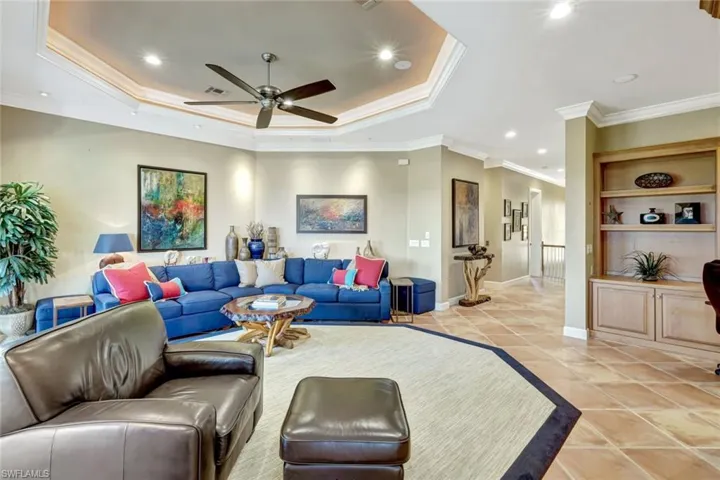 Living area featuring a tray ceiling, built in shelving, a ceiling fan, light tile patterned floors, ornamental molding